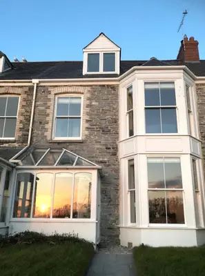a brick house with large windows with the sunset at The Moorings - Just a few metres from the sea! in Padstow