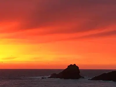 a sunset over the ocean with a rock in the water at The Moorings - Just a few metres from the sea! in Padstow
