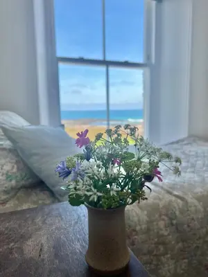 a vase with flowers on a table in front of a window at The Moorings - Just a few metres from the sea! in Padstow