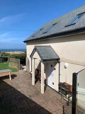 a white building with a black roof and a patio at Sunnyridge Cottage, Porthcothan Bay in Saint Ervan