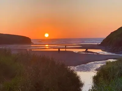 a sunset on a beach with people walking on the sand at Sunnyridge Cottage, Porthcothan Bay in Saint Ervan