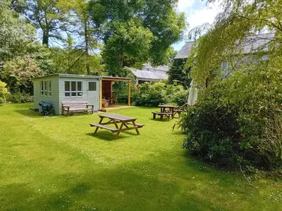 a picnic table and benches in a yard with a shed at Waterside Cottage in Penzance