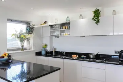 a kitchen with white cabinets and black counter tops at 6 Azure, Newquay in Newquay