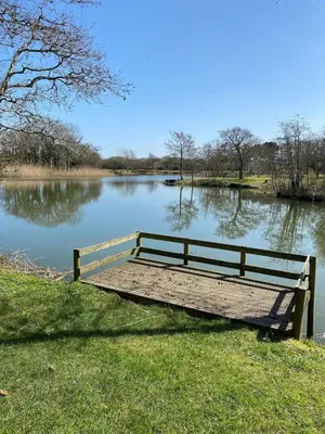 a wooden bench sitting on the side of a lake at Cosy 2 bed pet friendly holiday home Crantock Nr Newquay in Crantock