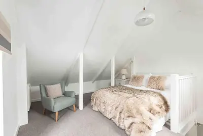 a white bedroom with a bed and a chair at The Old Shop in Withiel Village with private enclosed garden in Withiel
