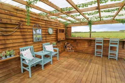 a porch with two chairs and a table and a pergola at Little Wren Cottage in Marazion