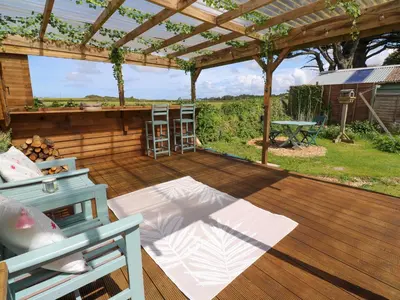 a wooden deck with a pergola and a table at Little Wren Cottage in Marazion