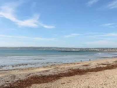 a beach with the ocean and buildings in the background at Little Wren Cottage in Marazion