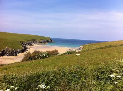 a green hillside with a beach and the ocean at Cubert Nr Newquay Traditional 16th century cottage in Cubert