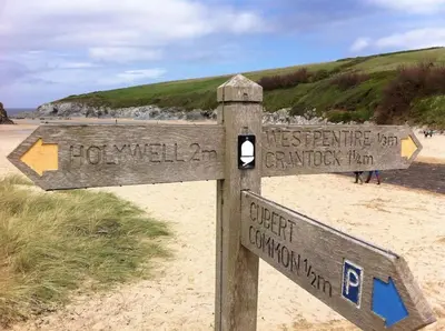 a wooden sign on a beach with people in the background at Cubert Nr Newquay Traditional 16th century cottage in Cubert