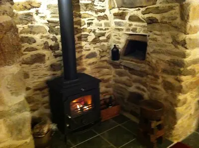 a stone fireplace with a stove in a room at Cubert Nr Newquay Traditional 16th century cottage in Cubert
