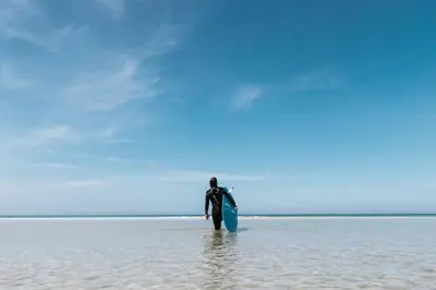 a man walking in the water with a surfboard at The Surf House Fistral in Newquay