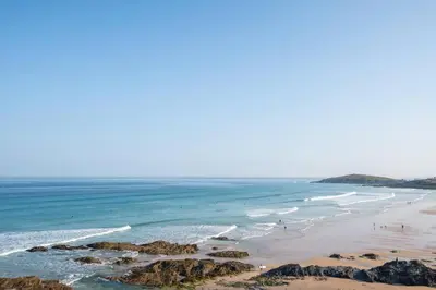 a beach with people walking on the sand and the ocean at The Surf House Fistral in Newquay