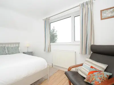 a bedroom with a bed and a chair and a window at Sea Drift in St Austell
