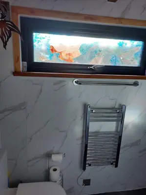 a bathroom with a window above a toilet and a mirror at Cosy Cornish Cabin in St Austell