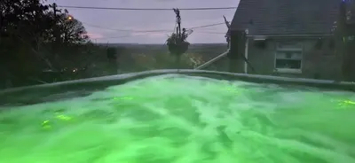 a bath tub filled with green water next to a house at Cosy Cornish Cabin in St Austell