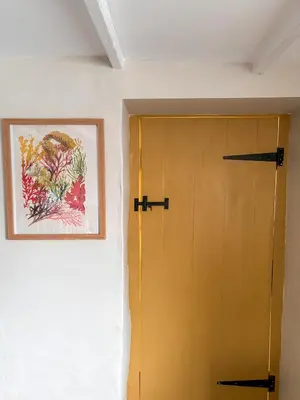 a yellow door in a room with a picture on the wall at April Cottage in Tintagel