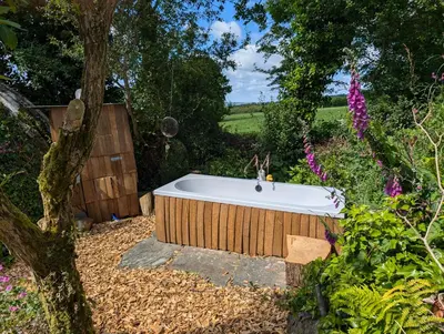 a bath tub in a garden with a tree at Dreckly cabin - Lydcott Glamping with Cornish sea views in Looe
