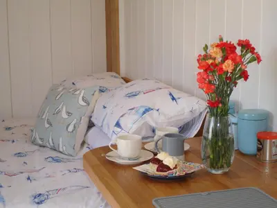 a table with a vase of flowers and a plate of food at Honeysuckle hut in Port Isaac