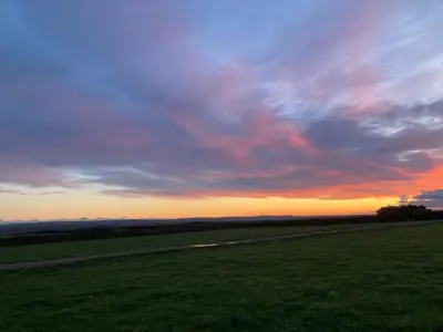 a sunset in a field with a grassy field at Honeysuckle hut in Port Isaac