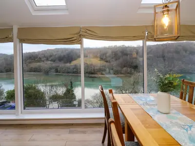 a dining room with a large window overlooking a lake at Anjoma in Looe
