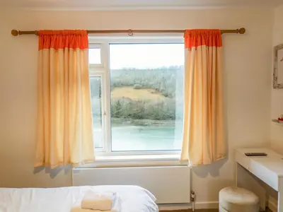 a bedroom with a window with orange curtains at Anjoma in Looe