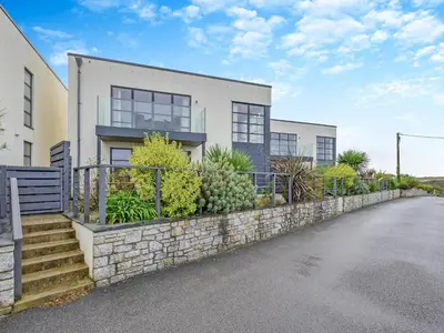 a white house with a stone retaining wall and stairs at 50 Degrees West in Perranporth