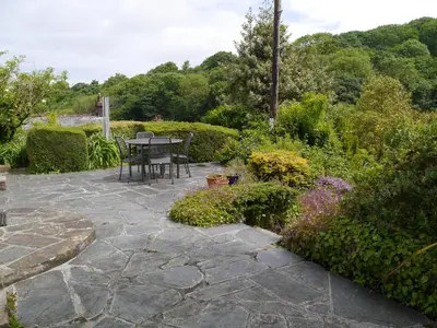a patio with a table and chairs in a garden at Cosy holiday cottage in Boscastle in Boscastle