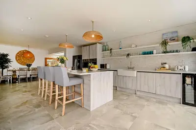 a kitchen with white cabinets and a island with bar stools at 3 Bed in Downderry oc-s29364 in Downderry