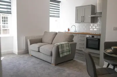 a living room with a couch and a kitchen at No.9 Priory House, Bodmin in Bodmin