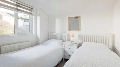 two beds in a white room with a window at The Lobster Pot in Port Isaac