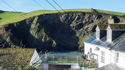 a white house with a mountain in the background at The Lobster Pot in Port Isaac