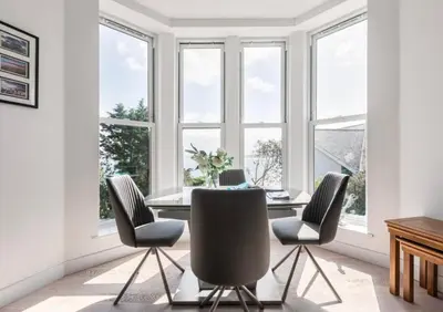 a dining room with a table and chairs and windows at Porthminster View Luxury Sea Views Balcony, Parking, Pool, Spa & Gym in St Ives
