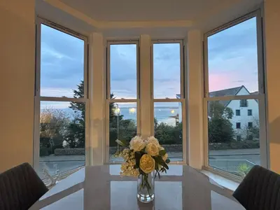 a vase of flowers on a table in front of a window at Porthminster View Luxury Sea Views Balcony, Parking, Pool, Spa & Gym in St Ives