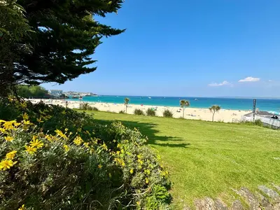 a view of the beach from a park with flowers at Porthminster View Luxury Sea Views Balcony, Parking, Pool, Spa & Gym in St Ives