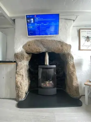 a room with a stone fireplace in a room with a tv at Bumblebee Cottage in Redruth