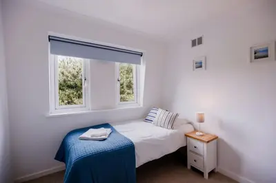 a white bedroom with a bed and two windows at St Anthony Cottage in Saint Mawes