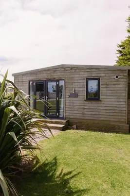 a small house with two windows in a yard at Bushwood - Free WiFi - Parking - Pet Friendly - On-site Activities in Helston