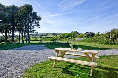 a picnic table sitting on the grass next to a gravel road at Wheal Rose - Hot Tub - Parking - Free WiFi - On-Site Activities in Helston