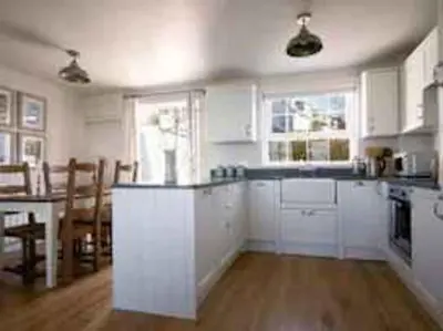 a kitchen with white cabinets and a table and a dining room at Castaway, Port Isaac Bay Holidays in Port Isaac