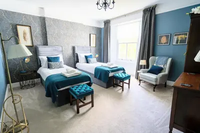 a blue bedroom with two beds and a chair at Stunning 4 bedroom house in Wadebridge, Cornwall - 2 living rooms and superking beds in Wadebridge