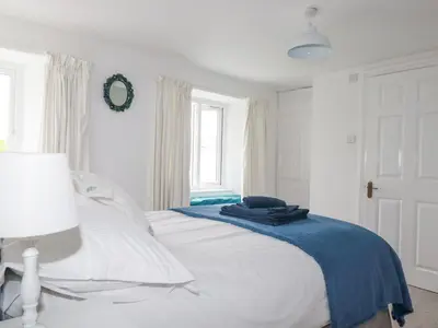 a white bedroom with a bed and a window at Langurra in Newquay