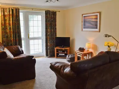 a living room with a leather couch and a television at Stone The Crows in Liskeard