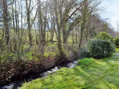 a stream in a field with trees and grass at Stone The Crows in Liskeard