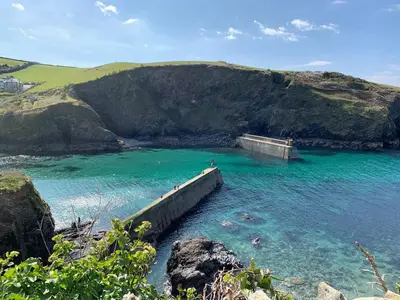 a pier in the water next to a mountain at Hillside in Port Isaac