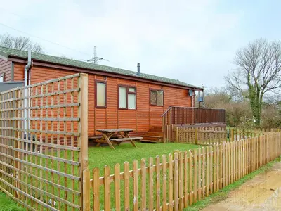 a wooden house with a fence and a picnic table at Rosewater Lodge in Saint Teath