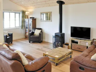 a living room with leather couches and a wood stove at Little Owl Lodge in Saint Columb Major