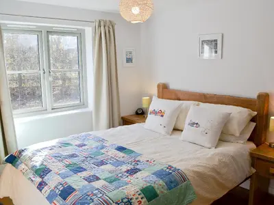 a bedroom with a bed with a quilt and a window at Little Owl Lodge in Saint Columb Major
