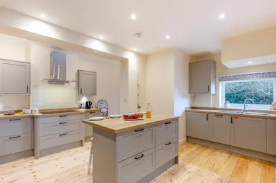 a large kitchen with white cabinets and a wooden floor at 3 Bed in Looe oc-s29266 in Looe