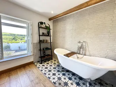 a white bath tub in a bathroom with a window at The Little Cottage at Porth in Newquay
